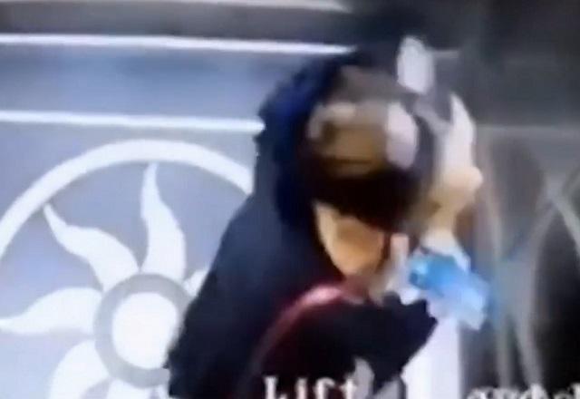 Mulher falando ao telefone dentro de elevador, em imagem capturada por câmera de segurança