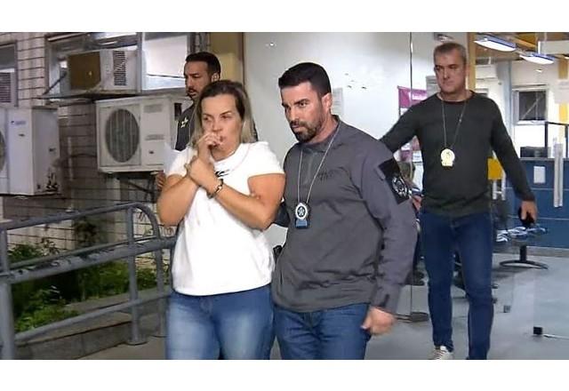 Mulher loira de blusa branca e calça jeans sendo encaminhada por três policiais