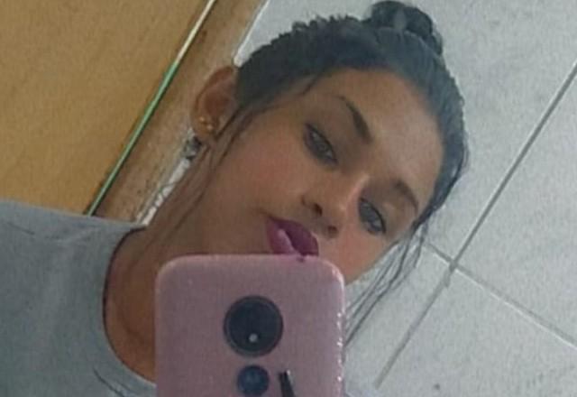 Mulher morena maquiada e com coque no cabelo tirando selfie no espelho com celular rosa