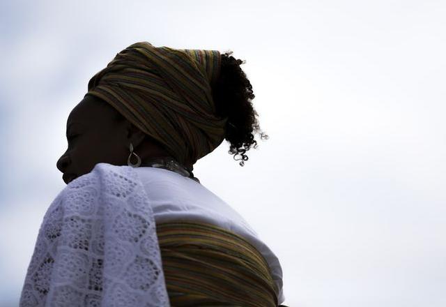 Mulher negra, de costas e vestes brancas, com céu ao fundo