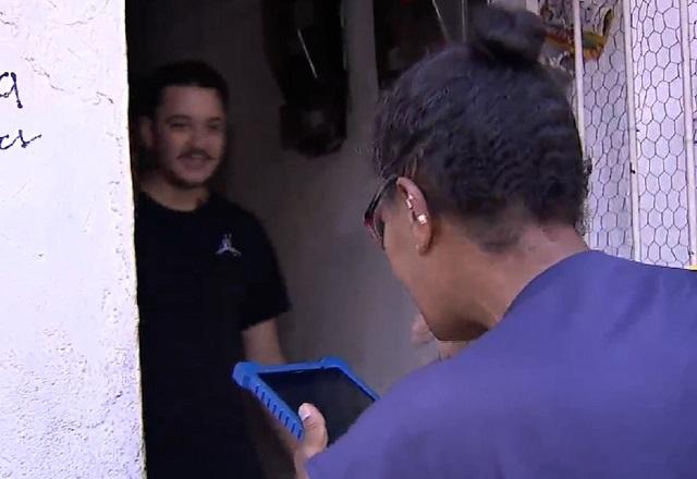 Mulher negra, de costas, segurando tablet ao atender homem branco em porta de residência