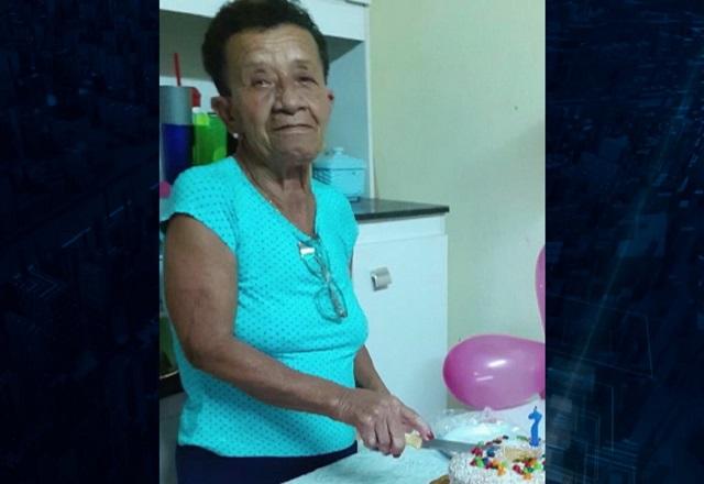 Mulher negra e idosa, de blusa azul, segurando faca prestes a cortar bolo