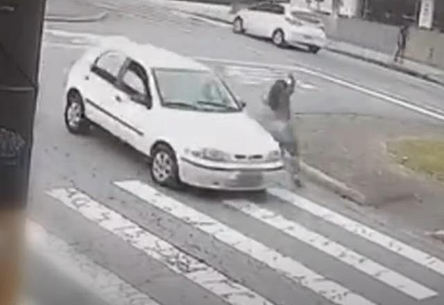 Mulher sendo atingida de raspão por carro, sobre faixa de pedestres de rua, durante o dia