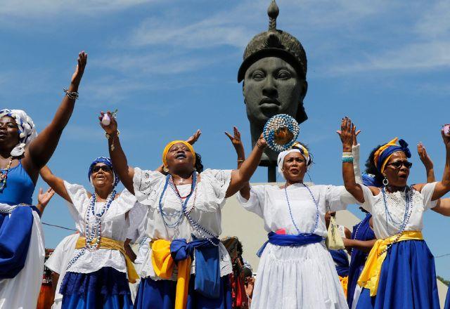 Mulheres com mãos ao alto em frente monumento do Zumbi dos Palmares