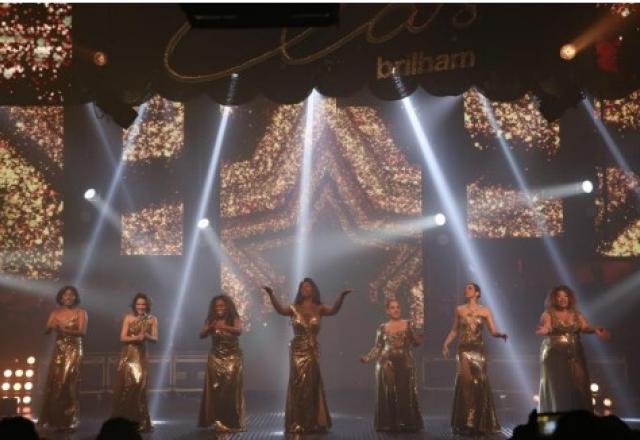 Mulheres vestidas de dourado cantam no palco