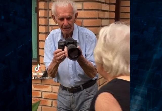 Nelson Miolaro, conhecido como vovô tiktoker, em cena com a companheira Nair, segurando uma máquina fotográfica