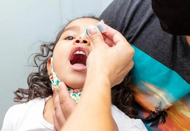 Profissional da saúde se prepara para despejar gota de vacina contra pólio na boca de criança (Divulgação/Opas)