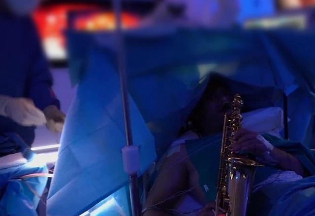 Paciente em cama de hospital, tocando saxofone, durante cirurgia no cérebro. com médico ao fundo fazendo o procedimento