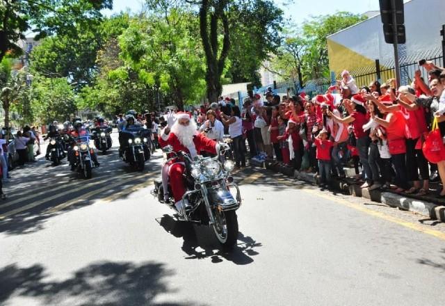 Papai Noel vestido de vermelho cumprimenta multidão em moto