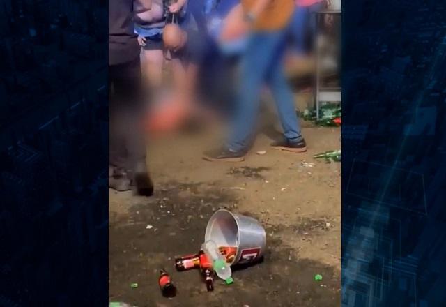 Pessoa ferida sendo atendida em chão de terra, durante show à noite, com balde de cerveja e garrafas espalhadas no chão