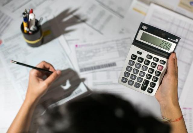 Pessoa segura calculadora e lápis sobre contas