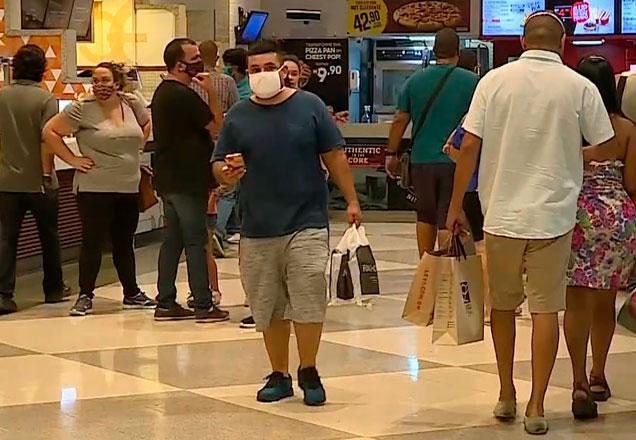 Pessoas caminham em praça de alimentação de shopping e carregam compras em sacolas