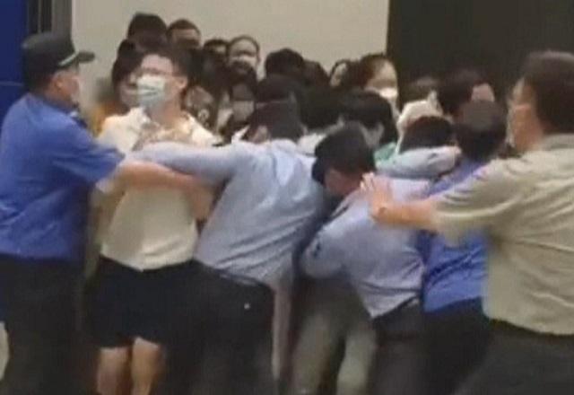 Pessoas chinesas forçando saída de porta, sendo contidas por seguranças