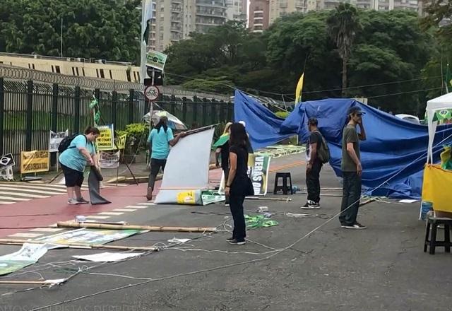 Pessoas desmontando barracas e retirando faixas em acampamento, no meio da rua