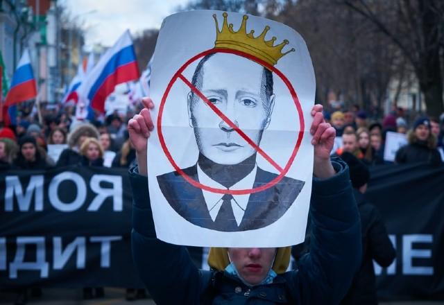 Pessoas manifestando contra Vladimir Putin; na foto, um cartaz contra o presidente da Rússia está em destaque