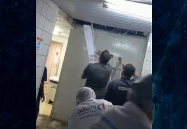 Pessoas observando e tentando conter queda de teto em corredor de hospital