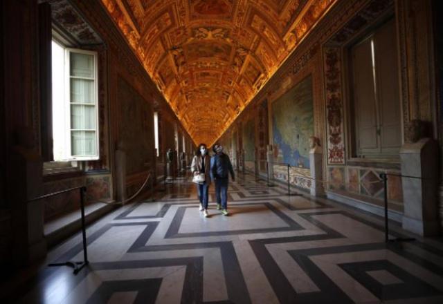 Pessoas usando máscara caminham por corredor de museu