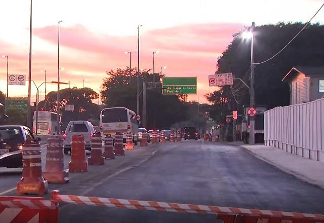 Pista de via asfaltada e interditada, com trânsito nas pistas ao lado, durante amanhecer