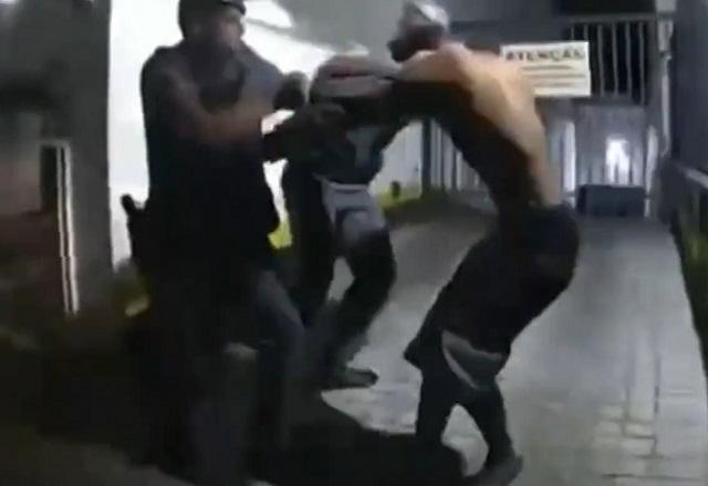 Policiais militares fardados tentando imobilizar homem negro durante abordagem
