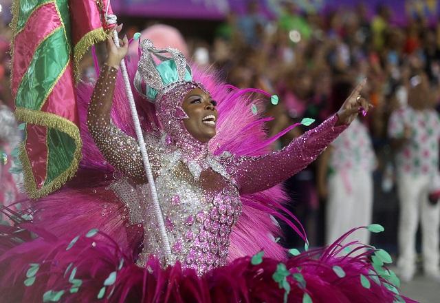 Porta-bandeira, fantasiada, sorrindo e apontando durante desfile no sambódromo