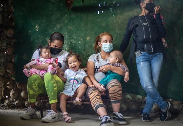 Refugiadas venezuelanas aguardam sentadas com filhas no colo atendimento em postos de ajuda na Colômbia