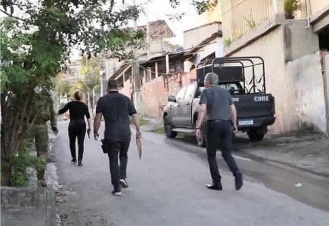Três policiais, com roupas pretas e de costas, subindo ladeira durante ação