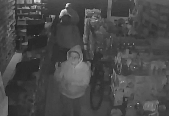 Trio de idosos encapuzados dentro de farmácia durante ação criminosa de roubo, flagrados por câmera de monitoramento do local, em imagem preto e branco