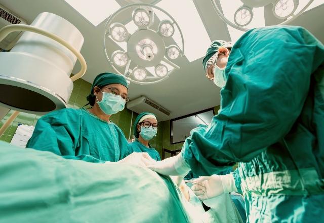 Um grupo de médicos vestidos com equipamentos de proteção individual verde estão em volta de uma mesa de cirurgia . Eles estão operando um paciente - Reprodução
