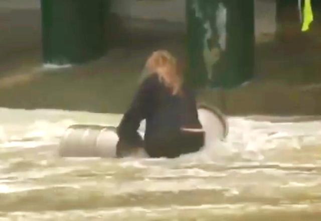 Uma mulher está dentro do mar, com a água na região da cintura, pegando dois barris de cerveja