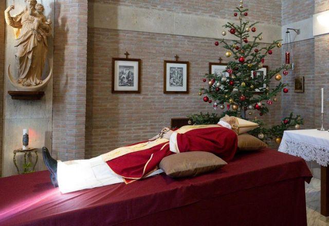 No local, Bento XVI encontra-se vestido com um manto vermelho e uma mitra, carregando um terço nas mãos | Reprodução/Vaticano