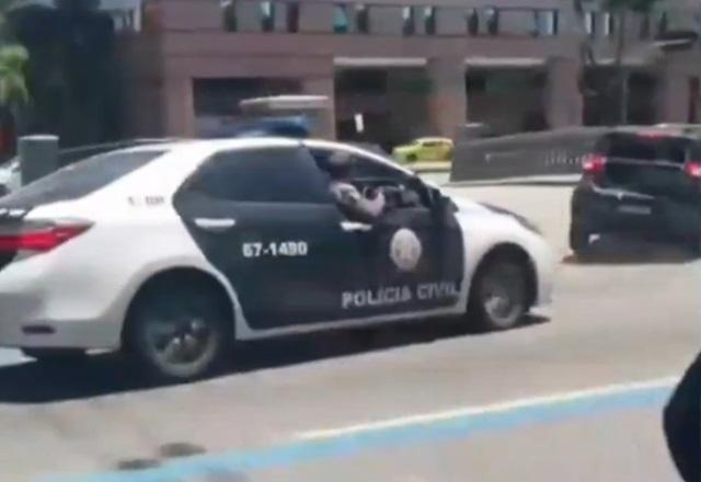 Viatura policial perseguindo outro carro no meio de avenida, durante a rua