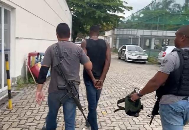 Um dos suspeitos, algemado, sendo conduzido por agente (Reprodução/WhatsApp)
