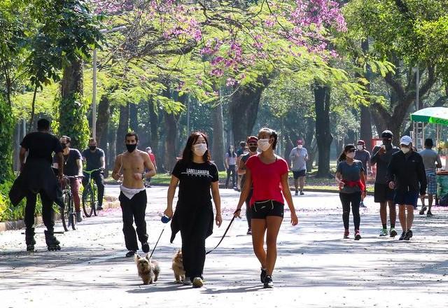 a imagem mostra pessoas se exercitando com máscara em um parque