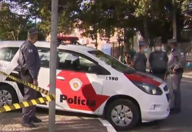 a imagem mostra um carro de polícia, policiais e uma fita isolando o local em que ocorreu a reação do policial