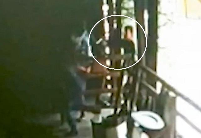 círculo branco destacando homem com arma em punho, apontando para outro, em porta de restaurante, durante o dia