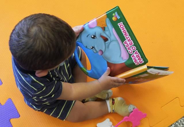 criança pequena lendo livro em creche