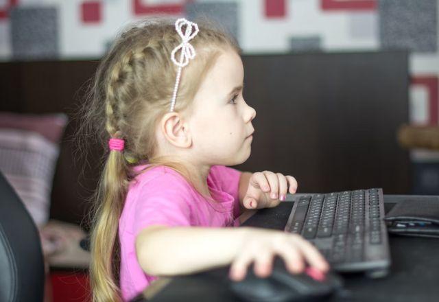 criança sentada mexendo no teclado e mouse do computador