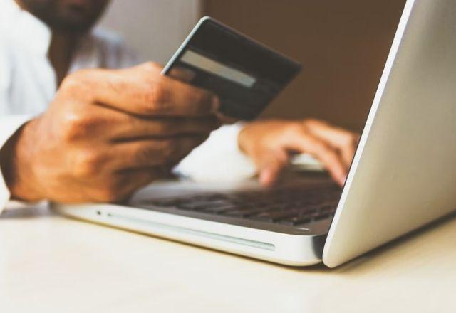 custo da internet sobe 8% no mundo - homem com cartão de credito na mão e acessando a internet