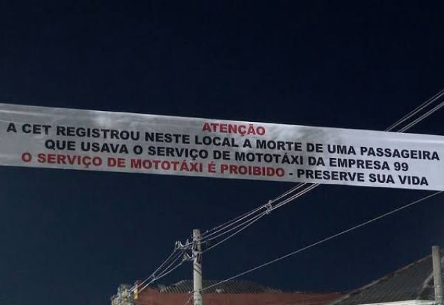 Faixa, que atravessa a avenida, diz: "A CET registrou neste local a morte de uma passageira que usava o serviço de mototáxi da empresa 99. O serviço de mototáxi é proibido - preserve sua vida" | Reprodução