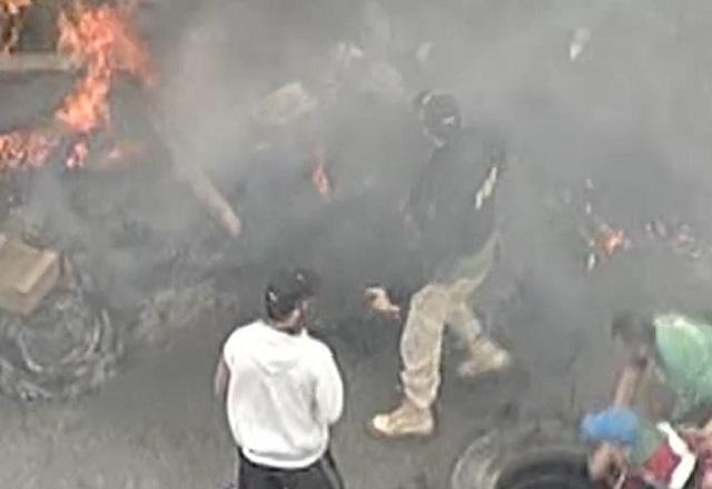 imagem do alto com policial rodoviário no meio de manifestantes e pneus pegando fogo em rodovia