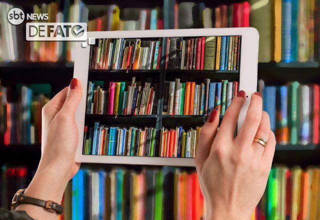 imagem mostra mãos de mulher segurando um tablet apontado e reproduzindo uma estante de livros