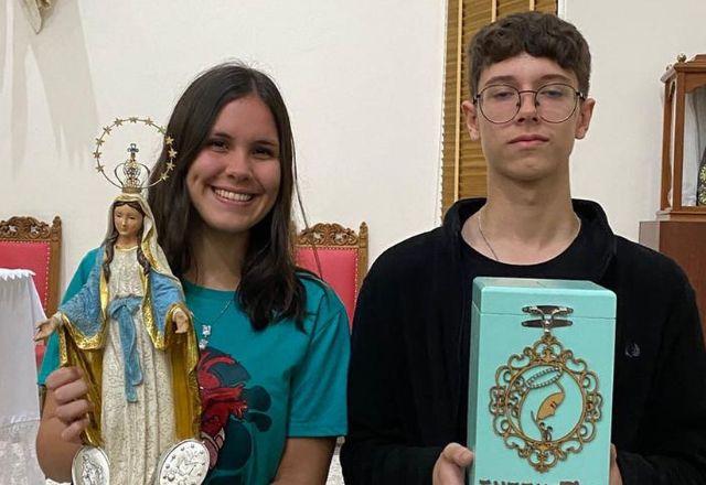 karoline segura a imagem de uma santa. luan está ao seu lado, segurando uma caixa azul