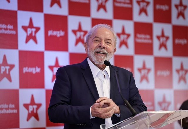 Lula fala ao microfone, à frente de parede com símbolo do PT (Reprodução/PT)