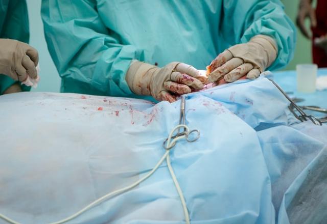 mãos de um médico efetuando uma cirurgia em um paciente coberto com uma manta azul