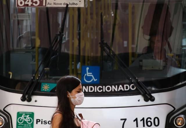 moça de máscaras em frente ônibus em SP