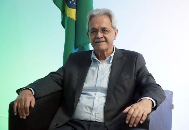 nilmário miranda sentado. atrás, uma bandeira do brasil