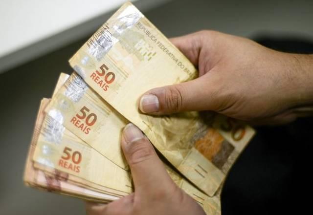 notas de 50 reais nas mãos de uma pessoa
