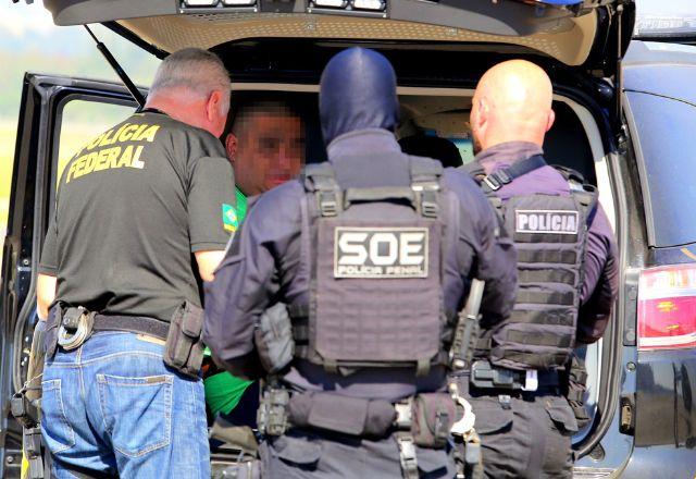 preso sendo colocado em viatura por três agentes