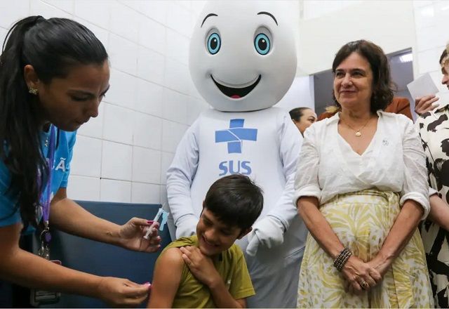 Criança recebendo vacina contra a dengue, acompanhado da ministra da Saúde e do Zé Gotinha (Fabio Rodrigues Pozzebom/Agência Brasil)